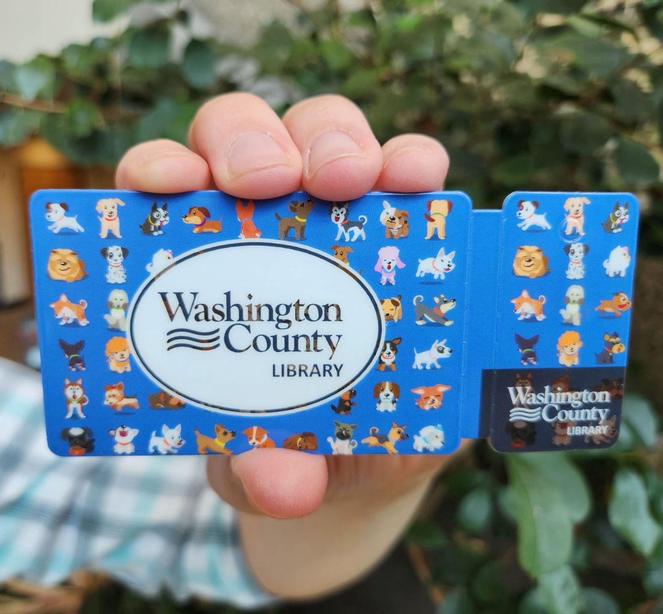 person holding a dog library card with leaves in the background