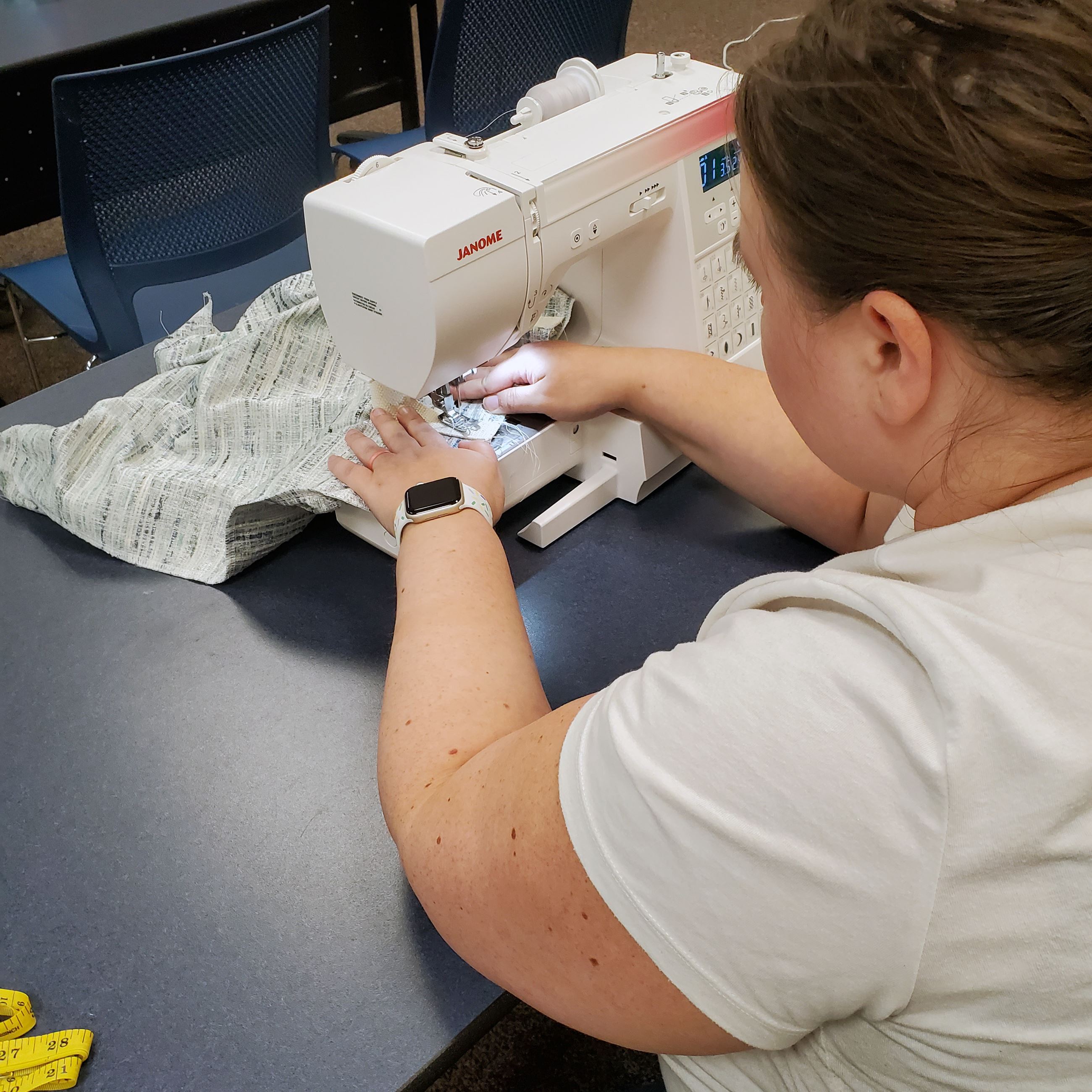 A library class participant sews a pillowcase using a white Janome sewing machine. 