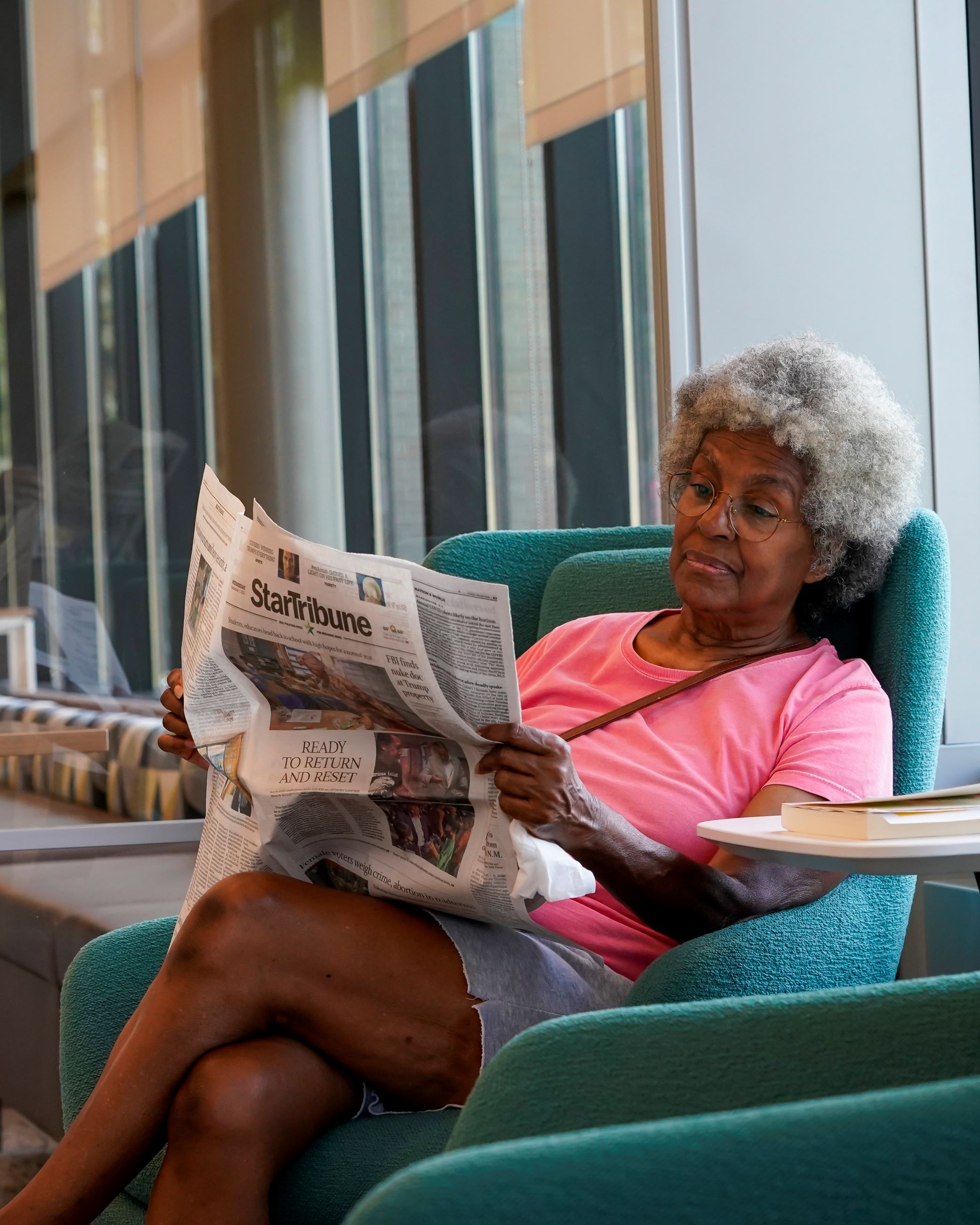 Woman sitting in a blue chair reading the Star Tribune