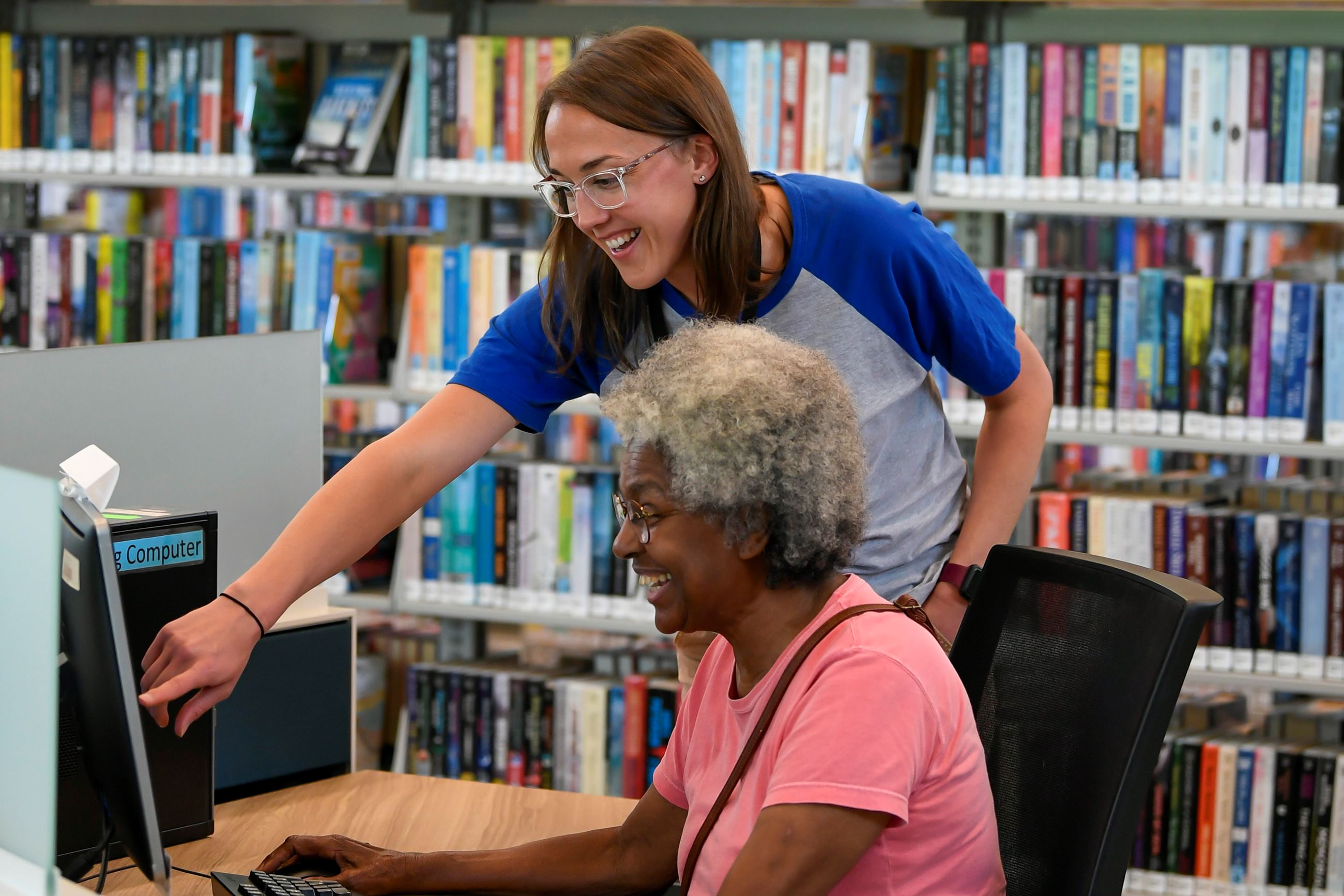 A library staff member helping a patron at a computer.