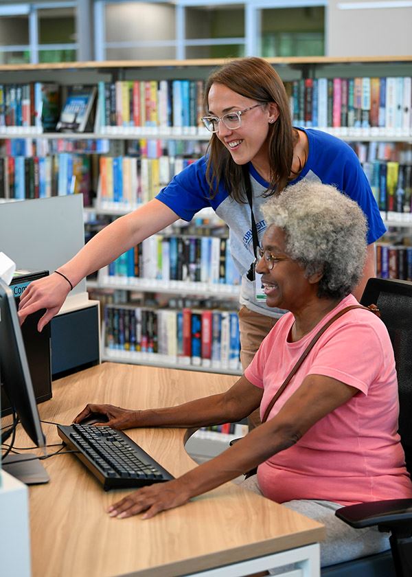 A library worker helping an older woman use a computer