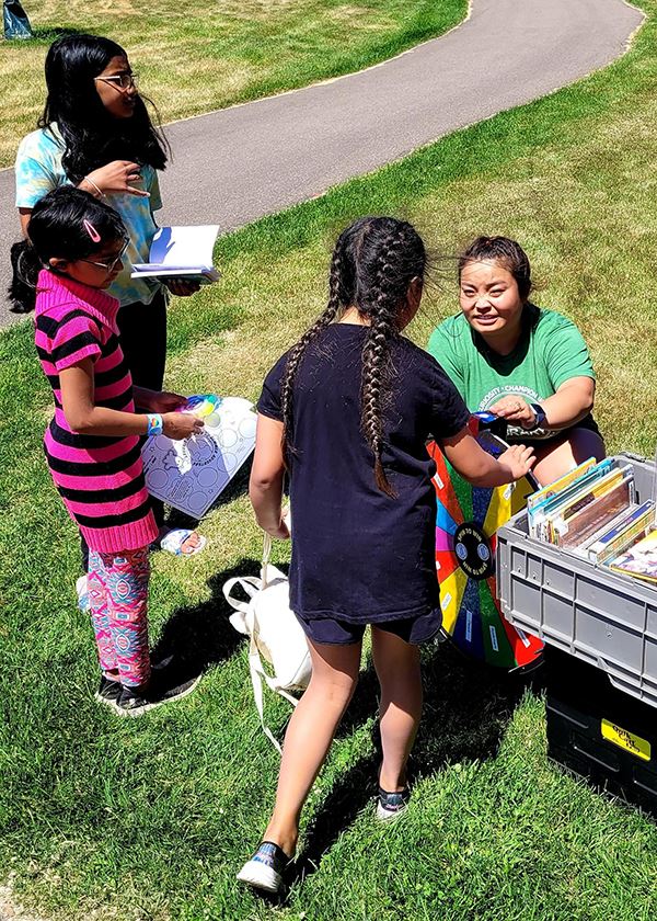Library staff member handing books to group of girls outside at a local park
